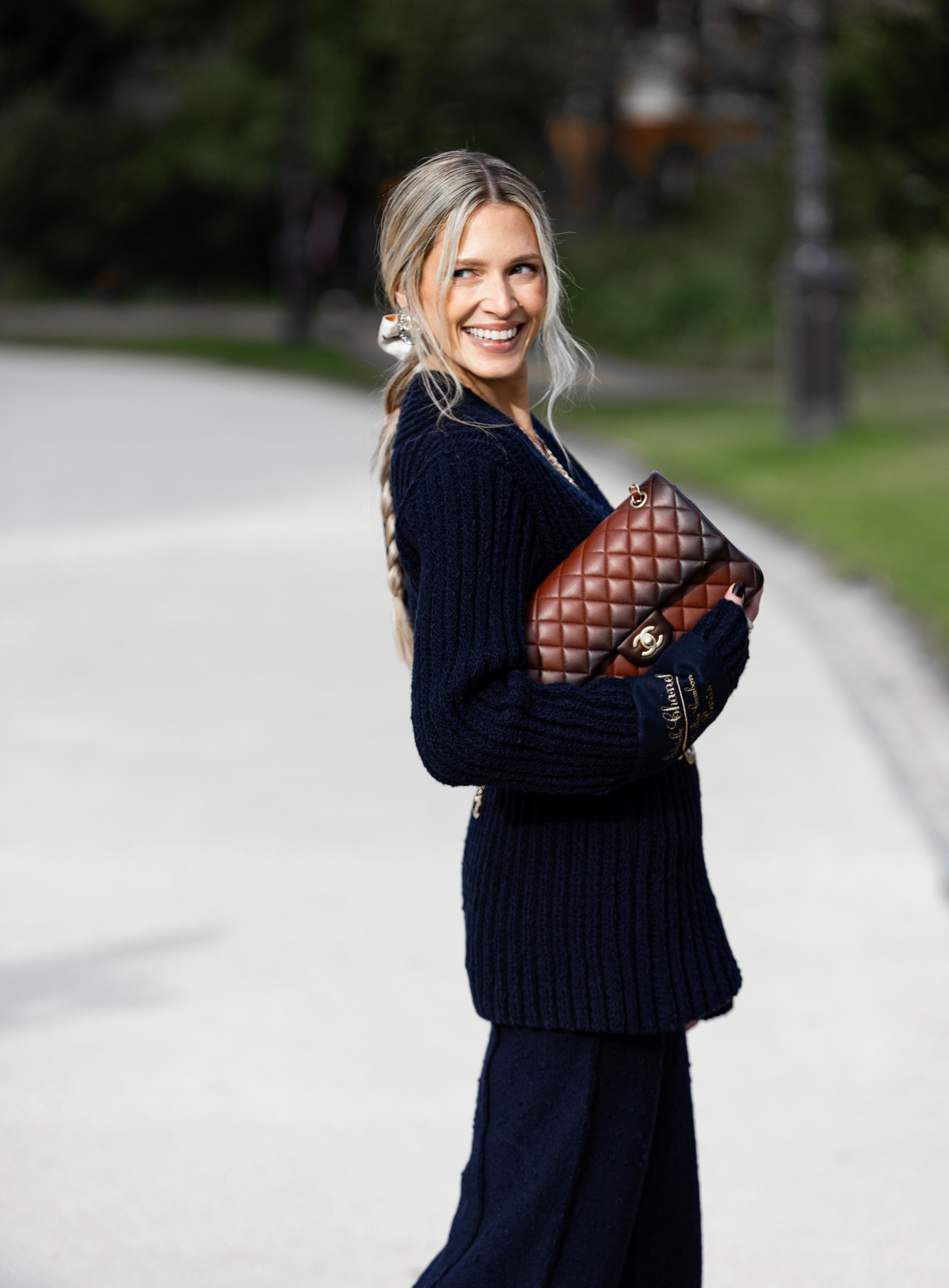 Woman in a knit sweater carrying a brown leather bag on a park pathway — editorial lifestyle photography, licensed via Pexels License